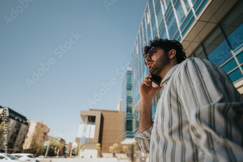 Confident male professional engaged in a conversation on his phone with city buildings in the background