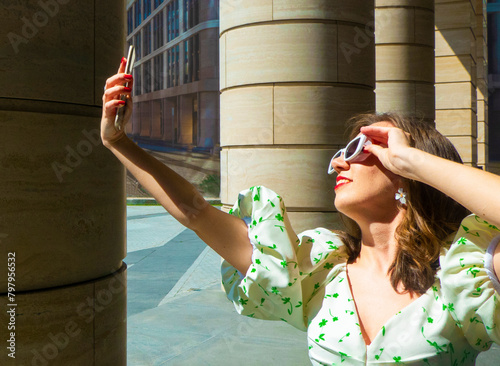 Joyful young caucasian woman winks, bites her tongue, takes selfie on phone. Blonde model wears hat in sunny weather. Positive emotions concept. High quality photo