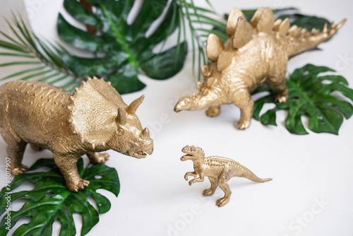 Fototapeta Naklejka Na Ścianę i Meble -  Golden dinosaur figurines and palm leaves on a white background.