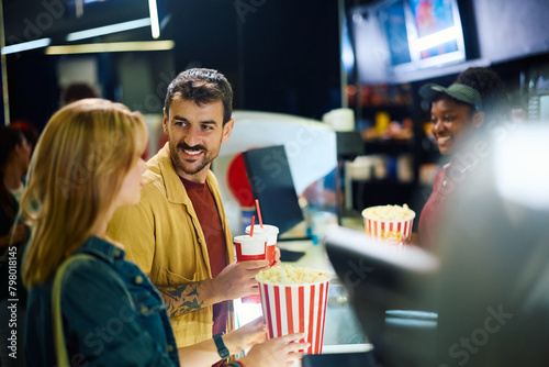 Smiling man and his girlfriend buying drinks and popcorn in cinema.