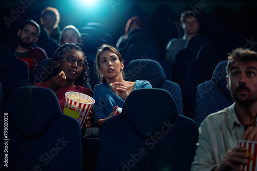 Young women watching suspenseful movie in cinema.