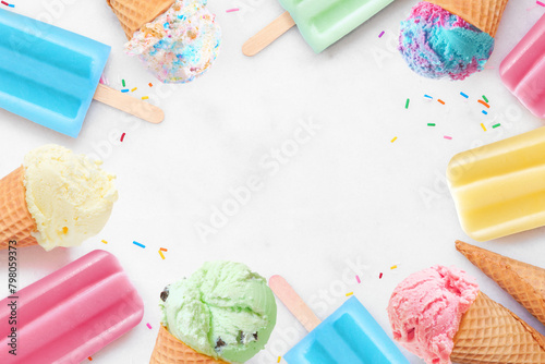 Variety of colorful pastel ice cream cones and popsicle summer frozen desserts. Top down view frame on a white marble background. Copy space.