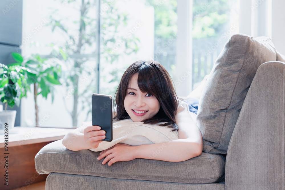 ソファでリラックスしてスマホを使う若い女性 ソファでリラックスしてスマホを使う若い女性