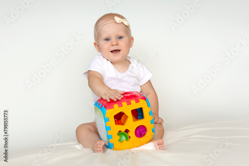 Baby on a white background with an educational toy cube with folding lid has different holes to fit.