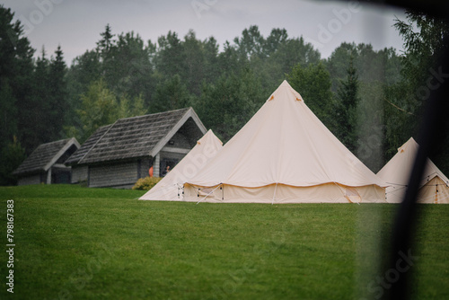 Dobele, Latvia - August 18, 2023 - A canvas bell tent on a rainy day, with pine trees and rustic cabins in the background.