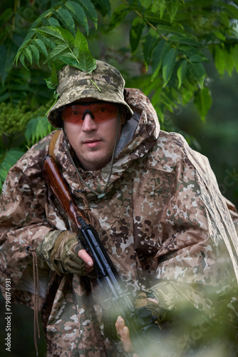 Ukrainian soldier in a protective camouflage military raincoat in the forest with a machine gun
