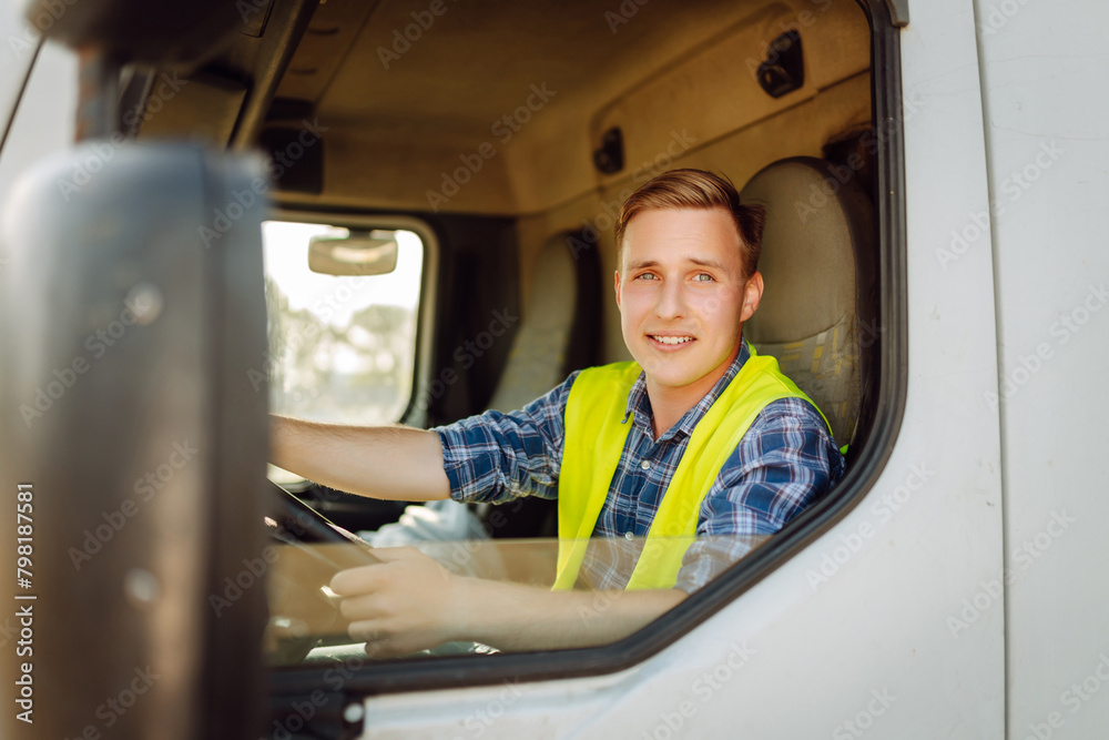 Handsome driver at the wheel of a truck at work. Driver or forwarder on truck and trailer, on a transshipment point. Transportation service. Handsome driver at the wheel of a truck at work. Driver or forwarder on truck and trailer, on a transshipment point. Transportation service.