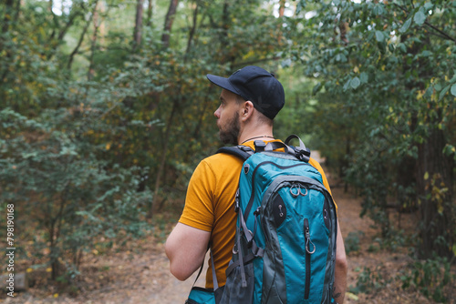 Half-length portrait of a young tourist man walking the forest path with a big travel backpack