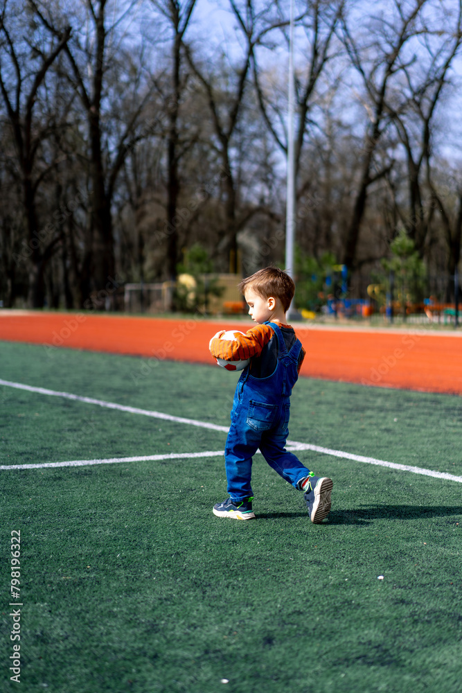 A young boy is holding a football on a field. The boy is wearing a blue outfit and he is enjoying himself