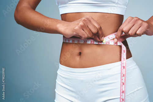 Girl, hands and tape on stomach in studio to measure weight loss or progress of diet and daily exercise. Woman, grey background and measurement for improvement of new prescription drug or tummy tuck.