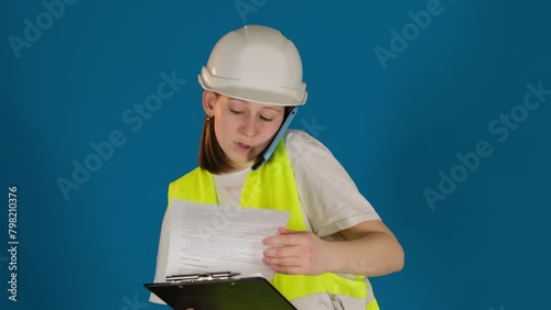 Worried female taskmaster talks via mobile phone reporting about problem on blue background. Woman builder with clipboard consults on call