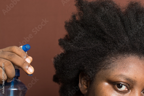 Water being sprayed on afro curly hair with shrinkage, woman with type 4c hair wetting her hair for detangling 