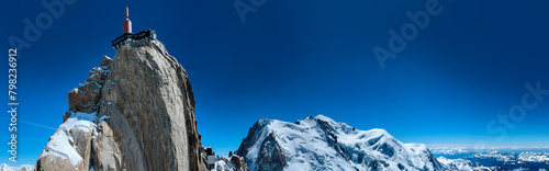 Haute-Savoie, France, 04-25-2024: blue sky and panoramic view of L’Aiguille du Midi (Needle at midday), the highest spire (3.842 m) of the Aiguilles de Chamonix, with the Mont Blanc massif peaks 