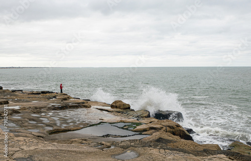 Fisher fishing in Mardel Plata coast Sea and gray sky Breaking waves on the rocks photo
