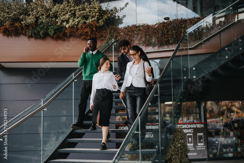 A group of multicultural business professionals are engaged in a conversation about marketing strategies while walking downstairs outside of a modern building.