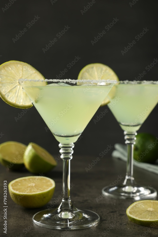 Delicious Margarita cocktail in glasses and limes on grey table