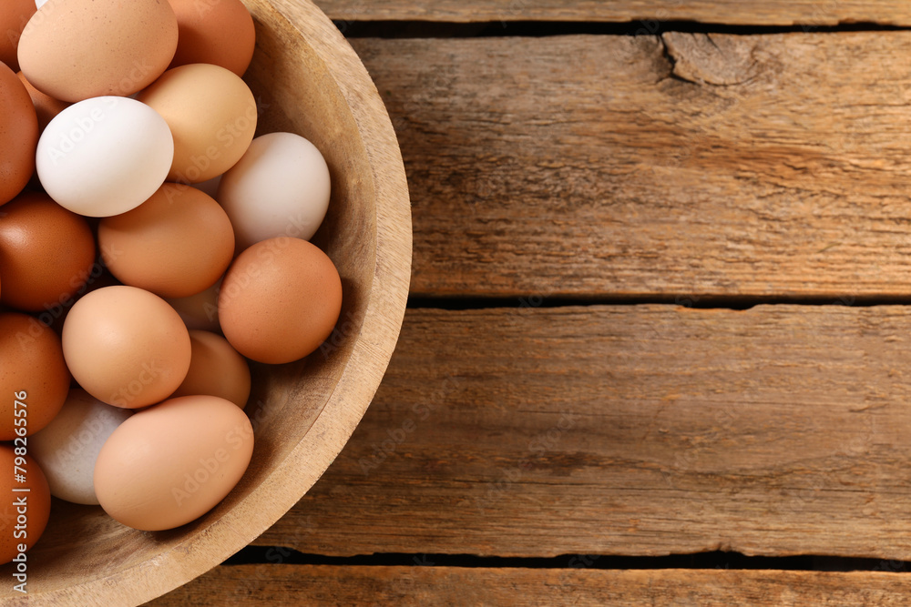 Chicken eggs in bowl on wooden table, top view. Space for text