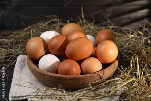 Fresh chicken eggs in bowl and dried hay on black wooden table