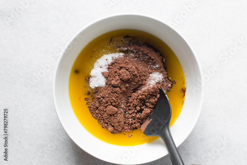 overhead view of melted butter white sugar and brown sugar cocoa powder in a white bowl, the process of making brownies, mixing butter and sugar to make brownies