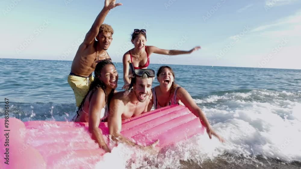 Funny group of multiracial friends with inflatable mat in to water enjoying summer vacation at the beach. Holidays lifestyle and friendship concept.