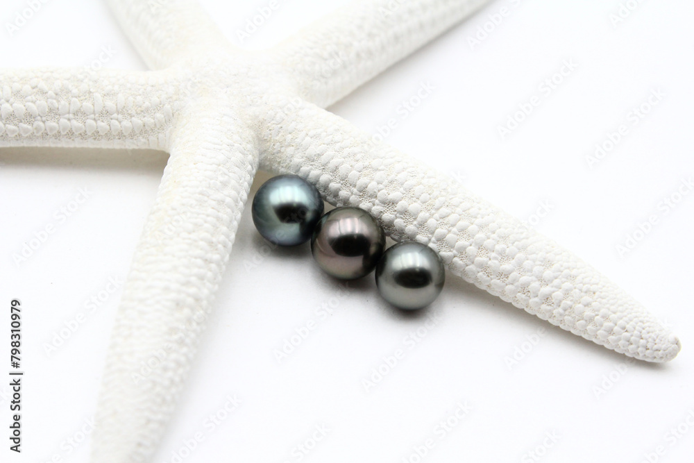 Expensive and luxurious Tahiti black pearls near a white starfish on white background, ready to be made into earrings, pendants or necklaces and sold in jewelry store. Expensive and luxurious Tahiti black pearls near a white starfish on white background, ready to be made into earrings, pendants or necklaces and sold in jewelry store.