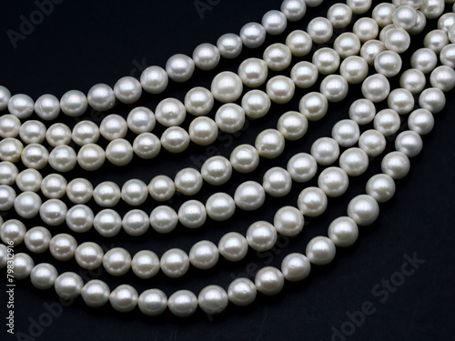 Chinese round freshwater white pearls on strands ready to become a necklace, some of the favorite materials for jewelry on black background. Lustrous nacre forms an organic gem.