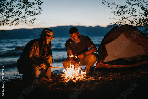 Two friends gather around a glowing campfire near a lake  preparing food as dusk settles  highlighting the beauty of the great outdoors.