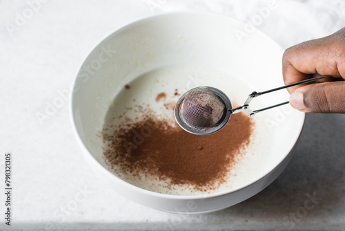 a silver strainer with Cocoa powder, sieving clumpy cocoa powder into batter photo