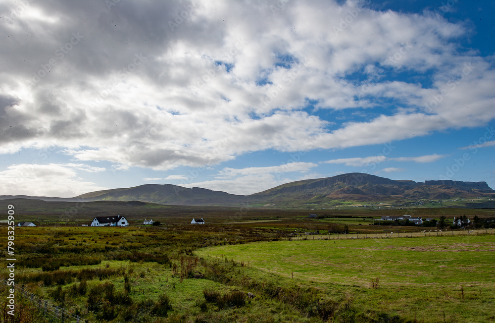 Fototapeta premium Farm houses on the Scottish hills in the isle of skye. Scotland, with Cuillin Mountains and orange clouds on backround in sunset light, Isle of Skye, Scotland