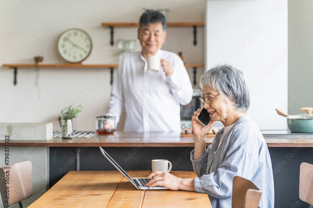 Obraz premium 家でパソコンを使う高齢者女性とキッチンにいる高齢者男性 