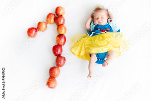 Flat lay picture of a 1 month baby with number made apples. Newborn baby girl in a princess outfit. Fairy tale costume on a baby. 1 month old with a number next to it