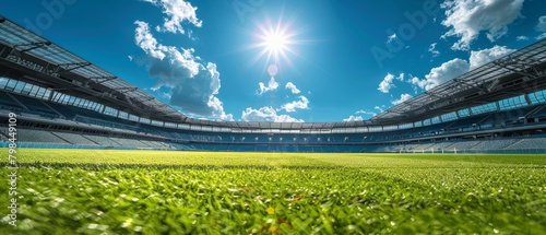 The photo shows a large, empty stadium with green field and bright blue sky.