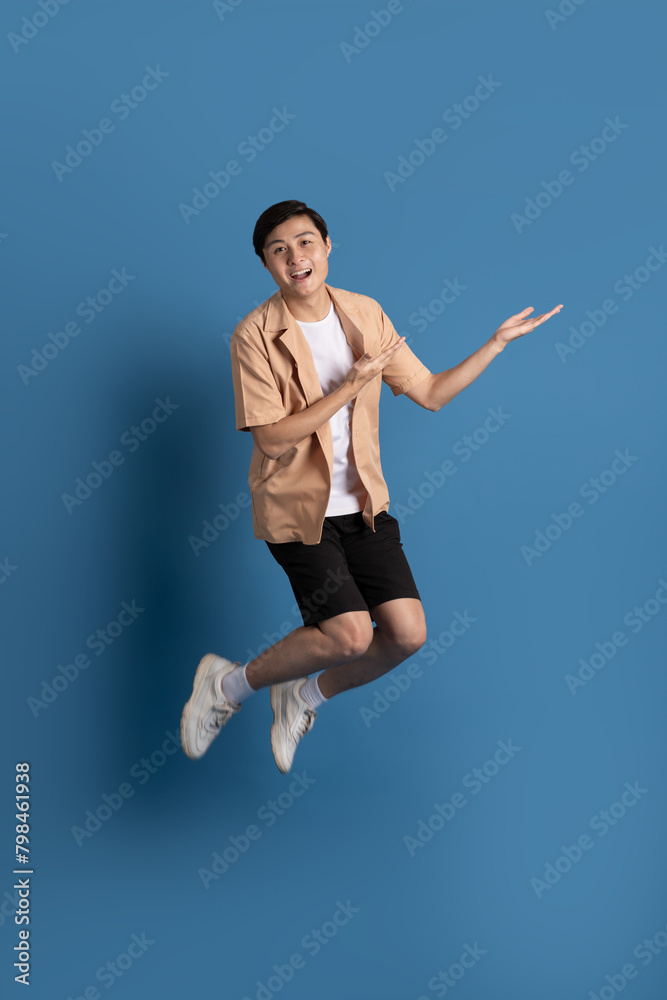 Portrait of Asian man posing on blue background, traveling in summer