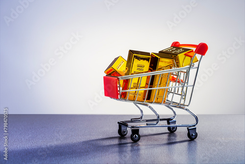 Shopping cart with gold bars on grey surface with place for text. Concept of security investment, trading, high demand purchasing, investment.