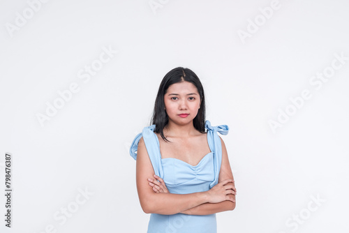 Young Asian woman in a powder blue dress, looking serious with arms crossed, isolated on white