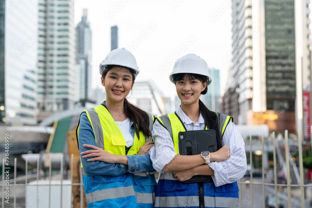 Two Asian female engineers looking at camera and standing arms crossed with a cityscape in the background Two Asian female engineers looking at camera and standing arms crossed with a cityscape in the background
