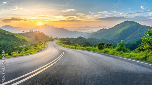 A sunrise view of a mountainous landscape and an asphalt roadway.