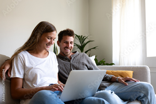 Happy young couple using laptop relaxing sitting on the sofa ordering online. Copy space.