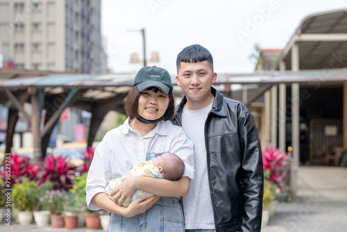 A mother and father in their 20s living in Yilan, Taiwan, are in a car holding a one-month-old Taiwanese baby.
台湾宜蘭に住む２０代の母親と父親が生後一ヶ月の台湾人の赤ちゃんを抱っこして宜蘭県羅東車站の前で立っている