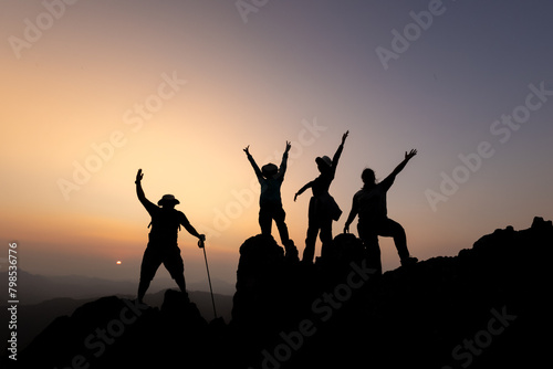 Silhouette of person hikers climbing up mountain cliff and one of them giving helping hand. People success, team work concept.