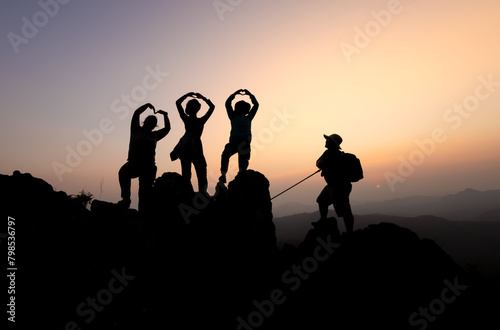 Silhouette of person hikers climbing up mountain cliff and one of them giving helping hand. People success, team work concept.