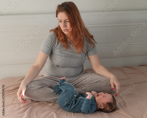 A Caucasian woman sits on a bed next to a crying baby. Postpartum depression.