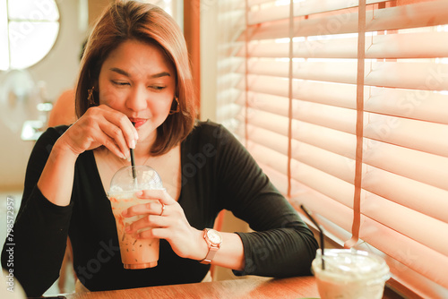 Cheerful asian young woman drinking coffee or tea enjoying it while sitting in cafe. Attractive happy asian woman holding a cup of coffee.