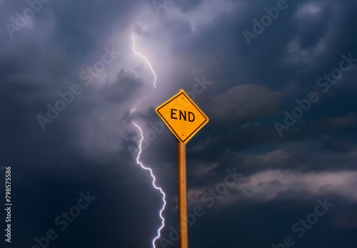 Yellow diamond shaped traffic sign with the word End written on it against a stormy cloudy sky with lightning
