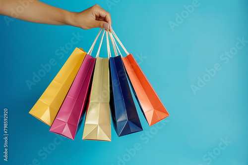 Woman's hand holds colored shopping bags on blue background. The concept of shopping and pleasant purchasing.