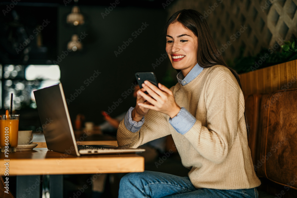 One beautiful female sitting in a bar indoors and using a laptop. Man in the background One beautiful female sitting in a bar indoors and using a laptop. Man in the background