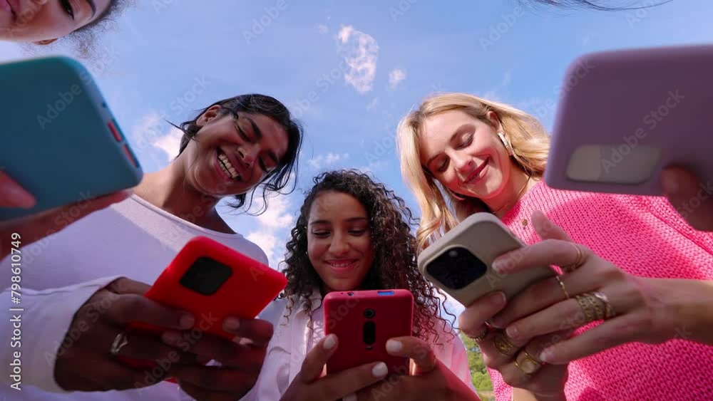 Young group of people using mobile phones together at city street. Diverse college student friends watching social media content on cell. Cellphone addicted people concept.
