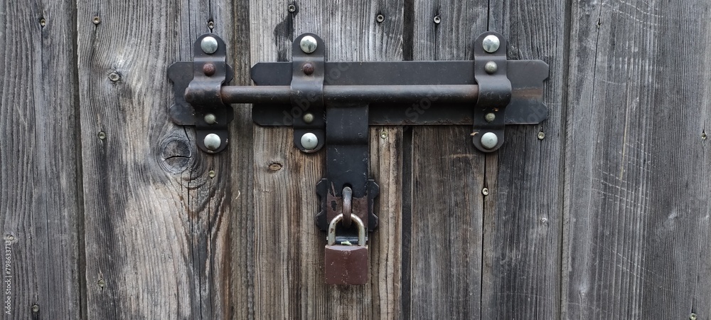 Metal lock on a wooden door, gate, old locking system Metal lock on a wooden door, gate, old locking system