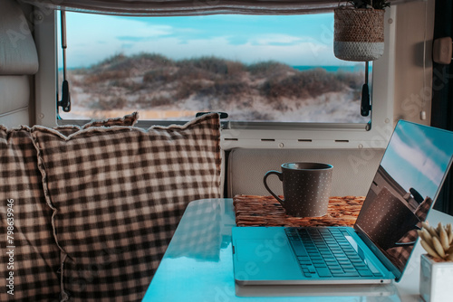 Alternative office for smart working and digital nomad vanlife lifestyle. One laptop on the camper van table with nature beach amazing beautiful view. Freedom lifestyle people. Online work business
