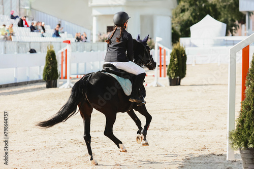 Show jumping competitions for children on ponies. A girl gallops over an obstacle on a Welsh black pony